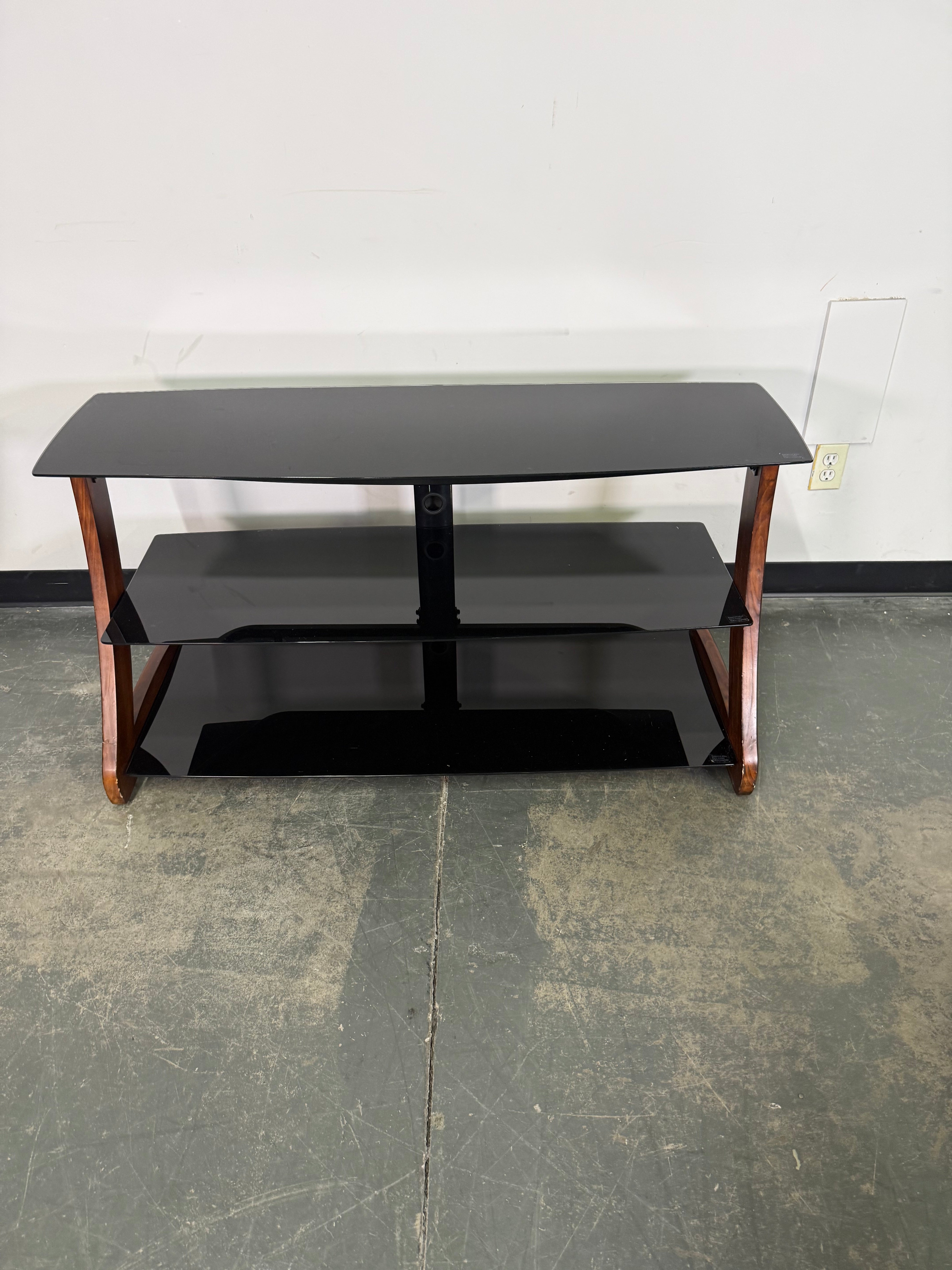 Black TV stand with wooden legs on a concrete floor.