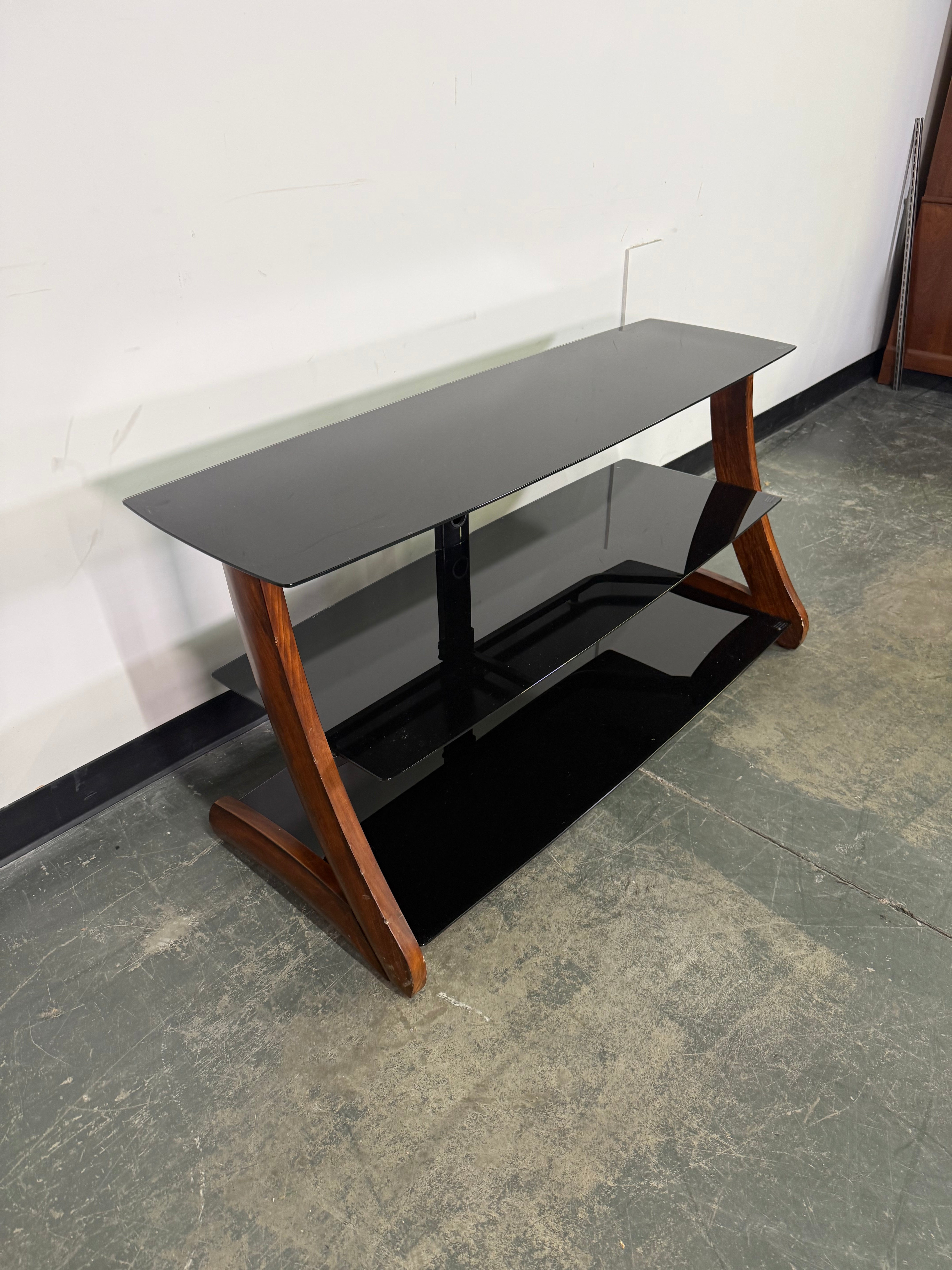 Black TV stand with wooden legs on a concrete floor.