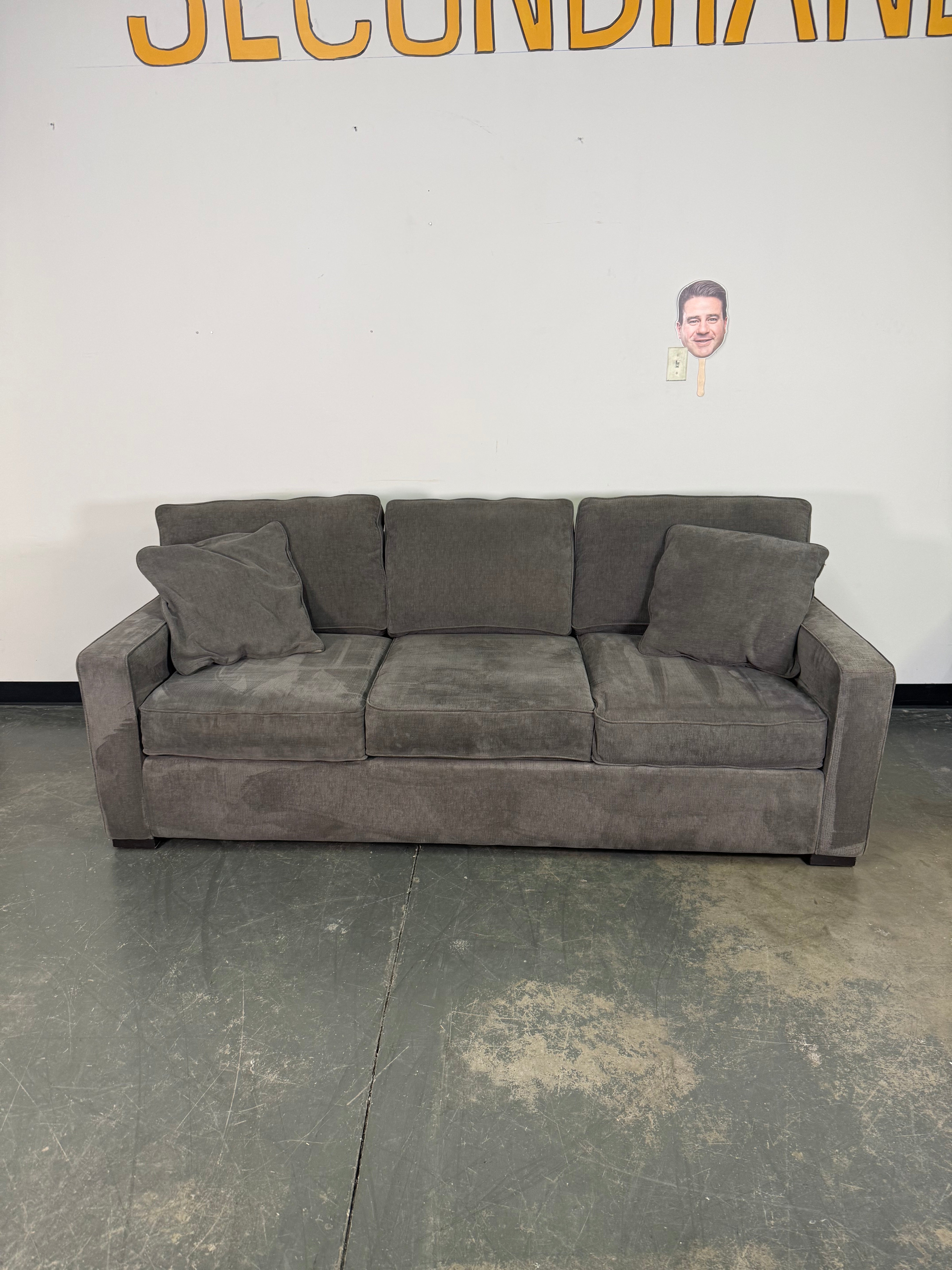 Gray sectional sofa against a plain wall with visible brand name.