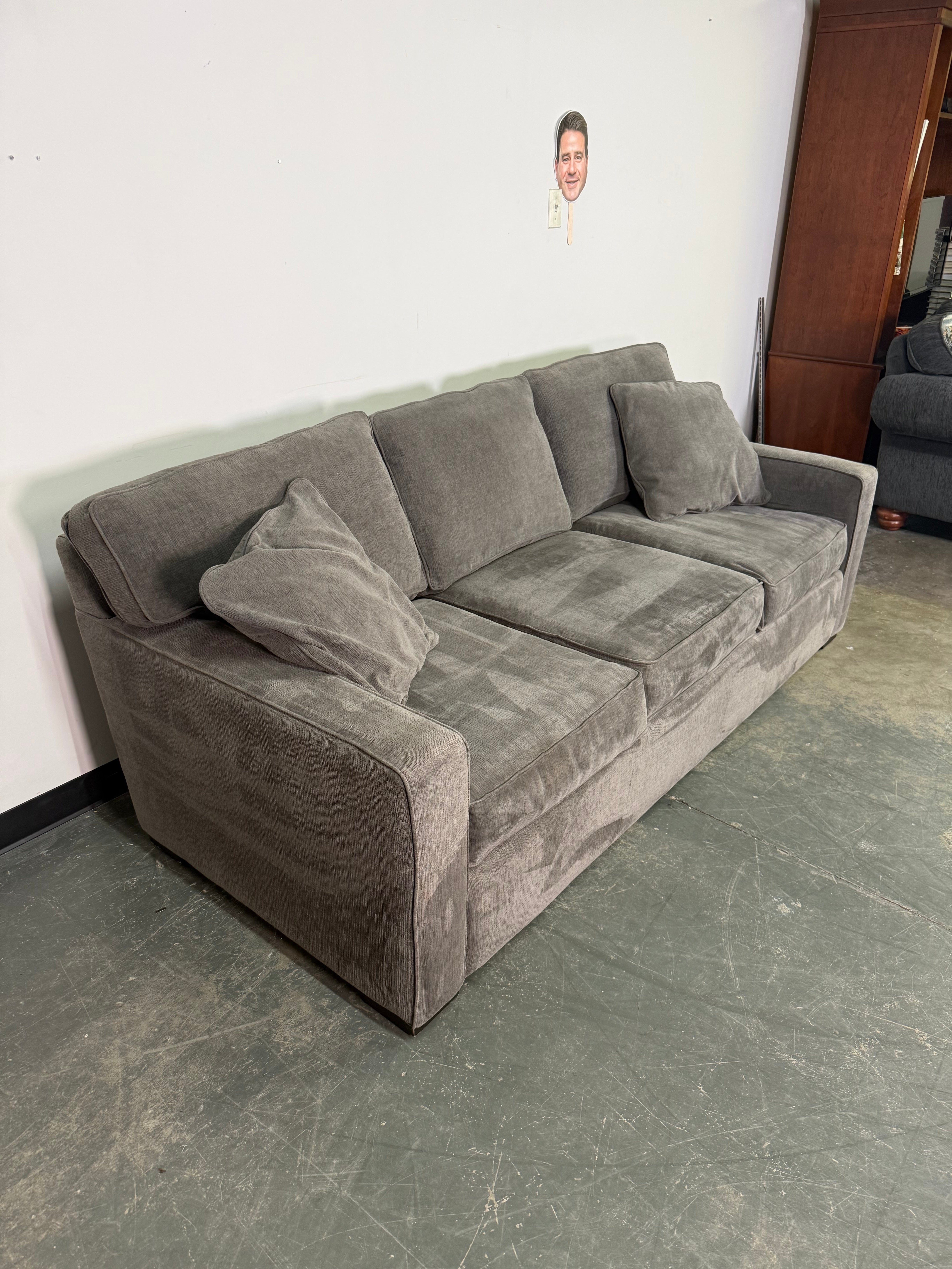 Gray sectional sofa against a plain wall with visible brand name.